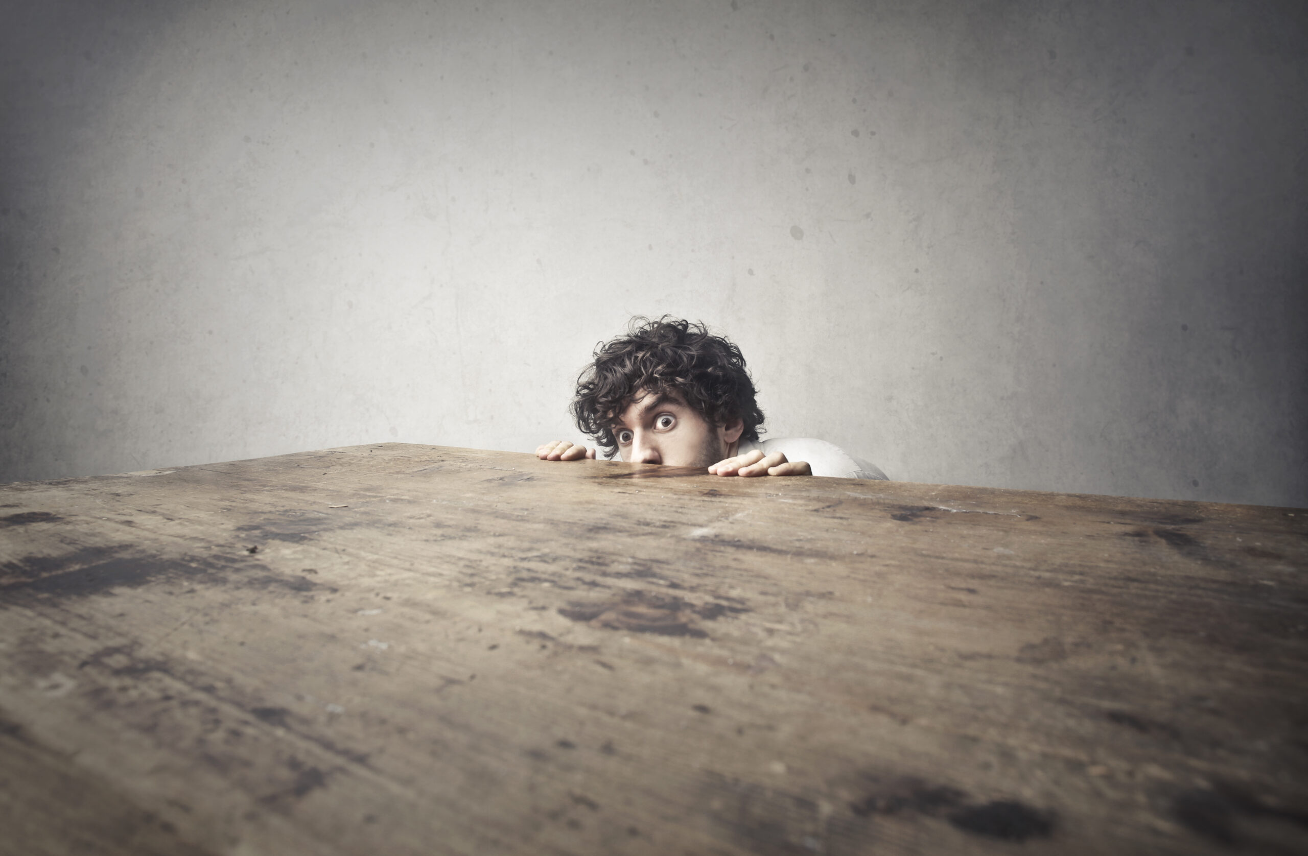 Scared man hiding behind wood table