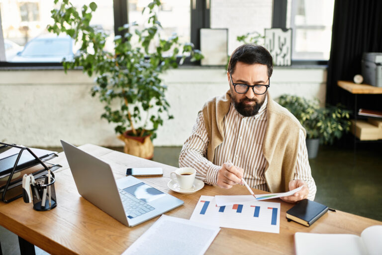 Good looking senior man reviews charts and graphs in a relaxed office setting while sipping coffee.