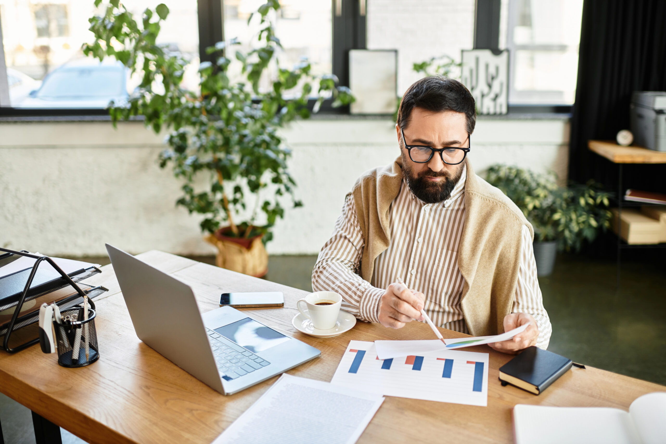 Good looking senior man reviews charts and graphs in a relaxed office setting while sipping coffee.